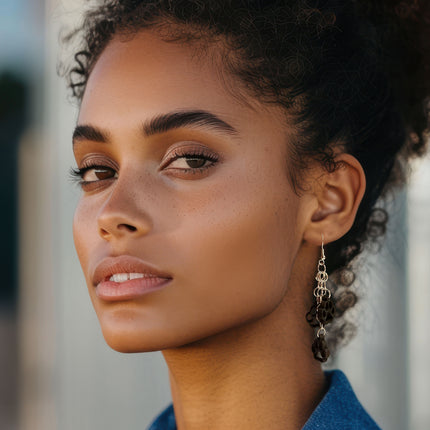 A close-up portrait of a woman wearing a dangling earring with silver-toned chain links and dark brown bead accents.