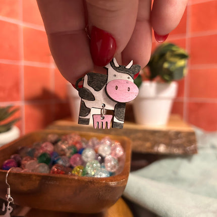 Hand-painted birchwood cow earring held between fingers showing painted detail
