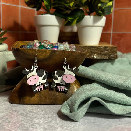 Hand-painted birchwood cow earrings displayed flat, black and white design with pink udder