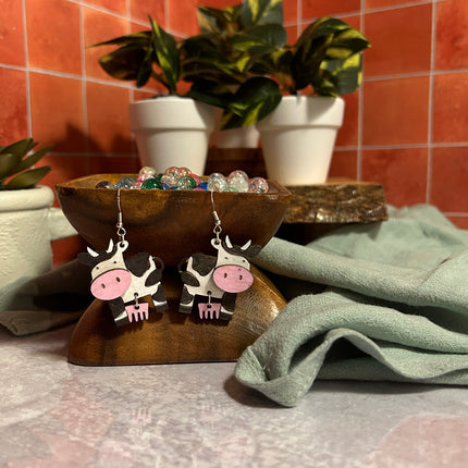 Hand-painted birchwood cow earrings with sterling silver fishhook ear wires, angled view