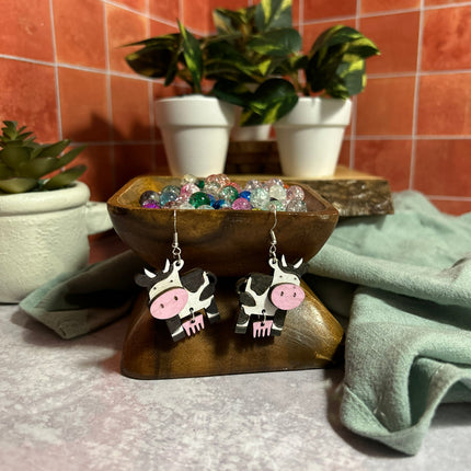 Hand-painted birchwood cow earrings on display, black and white cow with pink accents