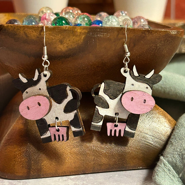 Close-up of hand-painted birchwood cow earrings with pink udders and sterling silver fishhook ear wires