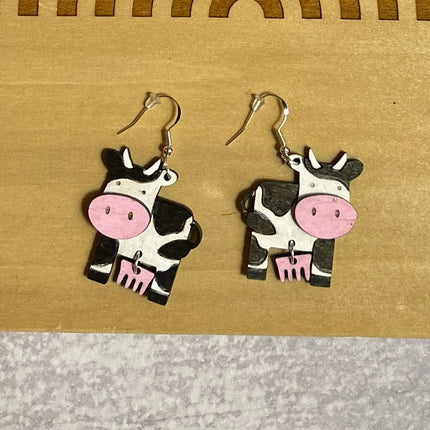 Close-up detail of hand-painted birchwood cow earring showing pink nose and udder