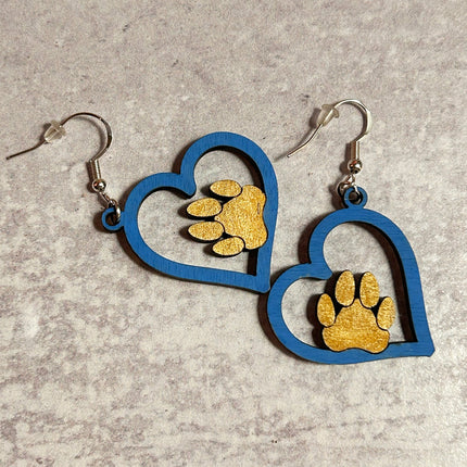 Close-up of blue hand-painted birchwood heart earrings with gold paw print charm, laid flat