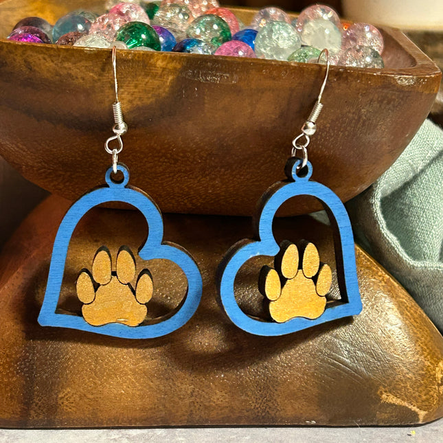 Close-up of blue hand-painted birchwood paw heart earrings displayed on a wooden bowl with decorative beads