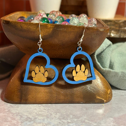 Blue hand-painted birchwood paw heart earrings, close-up angled view on wooden bowl stand