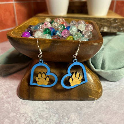 Blue hand-painted birchwood paw heart earrings on wooden bowl stand with colorful glass beads in background