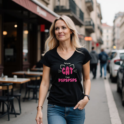 A woman walking on a city street wearing a black V-neck graphic T-shirt with a pink and white cat-themed design that reads 'Tell your CAT PSAPPSAPS'.
